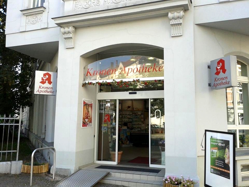 Außenansicht der Kronen Apotheke in Leipzig Außenansicht der Kronen Apotheke in Leipzig. Das Bild zeigt den Eingangsbereich der Apotheke mit automatischer Schiebetür, Apothekenschildern und barrierearmem Zugang über eine Rampe. Durch den Eingang ist der Verkaufsraum teilweise sichtbar.